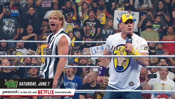 Logan Paul, wearing a black and white striped referee shirt, makes a playful expression while standing beside John Cena, who is wearing a white t-shirt and baseball cap, as they engage with an excited crowd at a WWE event. Fans can be seen in the background holding signs and cheering.
