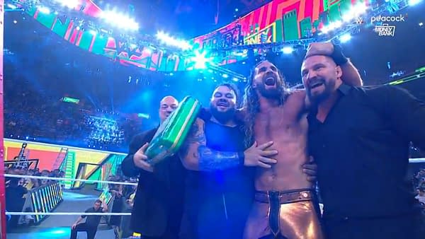 Seth Rollins celebrates winning the Men's Money in the Bank match, surrounded by teammates, with a green briefcase in hand and an arena full of lights in the background.