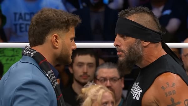 A close-up of two wrestlers, MJF and Mark Briscoe, engaged in a tense face-off on the AEW Dynamite stage, showcasing their intense expressions and competitive spirit. The audience is visible in the background, adding to the atmosphere.