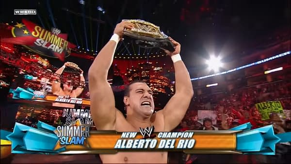 A man with a muscular build, Alberto Del Rio, triumphantly raises the WWE Championship belt above his head, celebrating victory at SummerSlam 2011, as a vibrant crowd cheers in the background and the SummerSlam logo is displayed prominently.