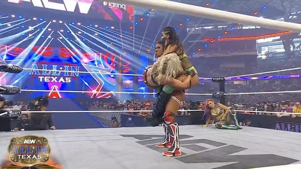 Athena performs a wrestling move, holding two women in the ring during the AEW All In Texas Casino Gauntlet match, with dramatic lighting and an excited crowd in the background.