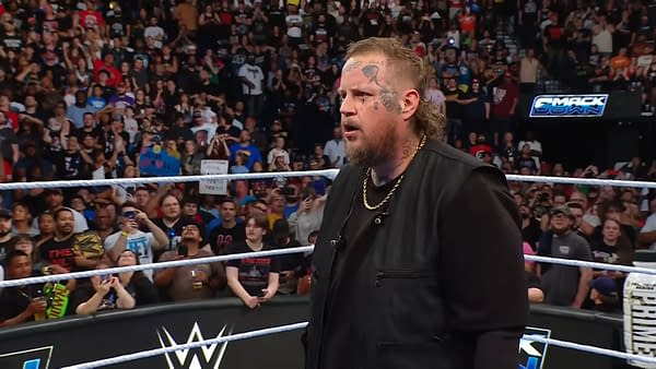 Jelly Roll, a global entertainment superstar, stands in the WWE SmackDown ring with a serious expression, surrounded by an excited crowd holding signs and taking photos.