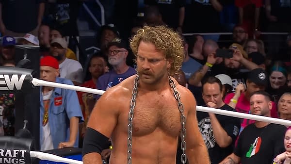 Hangman Adam Page stands confidently in the wrestling ring during AEW Dynamite, wearing a chain around his neck, with a focused expression while fans watch in the background.