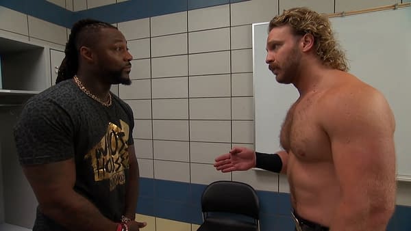 Swerve Strickland and Hangman Adam Page engage in a serious discussion backstage at AEW Collision, with Strickland in a patterned shirt and Page shirtless with a championship belt.