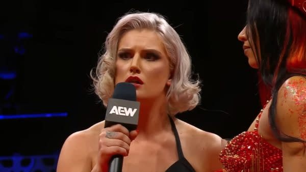 A female wrestler, Toni Storm, is holding a microphone and has an intense expression as she confronts another wrestler, Mercedes Moné, during a segment on AEW Dynamite. The scene captures a moment of heightened tension ahead of their upcoming match.
