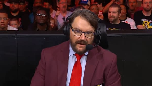 Tony Schiavone, wearing a maroon blazer and a red tie, speaks into a microphone while discussing Hulk Hogan's death on AEW Collision. The crowd is visible in the background, showing various reactions.