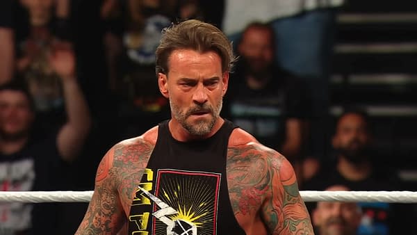 A muscular man with tattoos, CM Punk, appears on WWE Raw, wearing a black tank top with a graphic design. He looks intense, engaging with the audience.