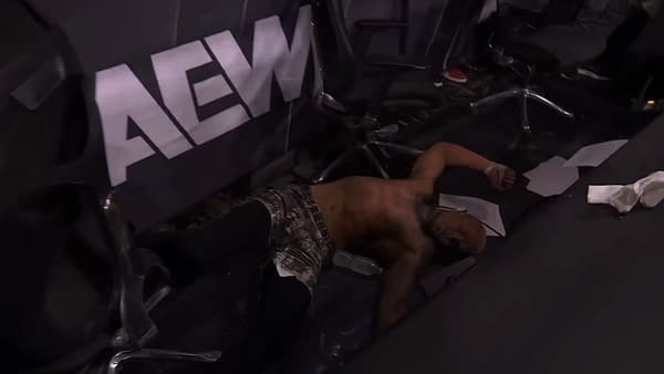 Darby Allin lies on the ground amid debris from the announce table, suggesting he has just been thrown out of the wrestling ring by Claudio Castagnoli during a match.