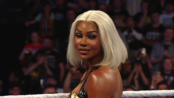 Jade Cargill stands in the wrestling ring on WWE SmackDown with a confident expression, wearing a black and gold outfit. The background features an audience applauding and cheering for her performance.