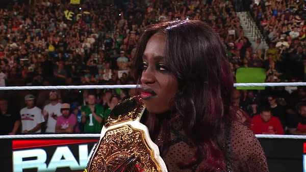 WWE superstar Naomi holds her championship belt while announcing her pregnancy on WWE Raw, amidst a cheering crowd. Her expression conveys a mix of emotion on this significant moment.