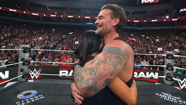 AJ Lee and CM Punk share a warm embrace in a cheerful WWE Raw setting, with a lively audience in the background.
