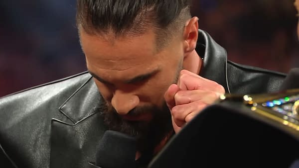 Seth Rollins is shown with his head bowed, appearing deep in thought as he prepares to deliver a scripted line during a promo on WWE Raw, wearing a black leather jacket. His hand is clenched near his face, showcasing a moment of concentration.