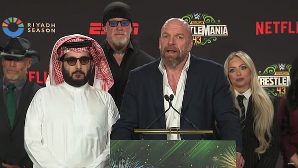 A press conference event featuring several speakers, including individuals in traditional Middle Eastern attire and iconic wrestling figures, discussing WWE WrestleMania 43 taking place in Saudi Arabia.