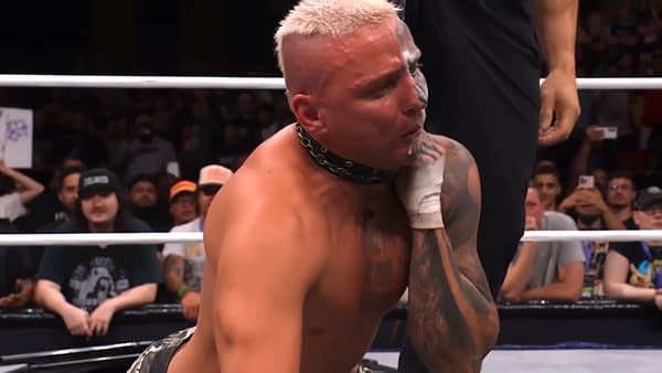 A wrestler, Darby Allin, appears to be in distress as he is choked out in the ring after a wrestling match on AEW Dynamite. The audience can be seen in the background, capturing the dramatic moment on their phones.