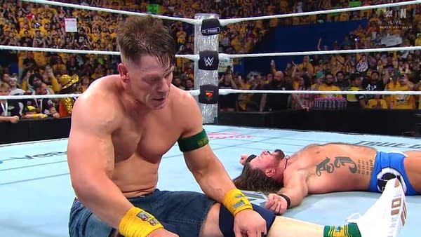 John Cena, appearing exhausted but triumphant, sits on the mat after a grueling match against AJ Styles at WWE Crown Jewel in Perth, surrounded by a cheering crowd.