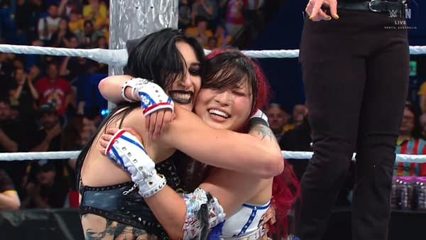 Rhea Ripley and Iyo Sky embrace in a joyful hug after their victory at WWE Crown Jewel in Perth, Australia. Both wrestlers are expressing happy emotions in the celebratory moment.