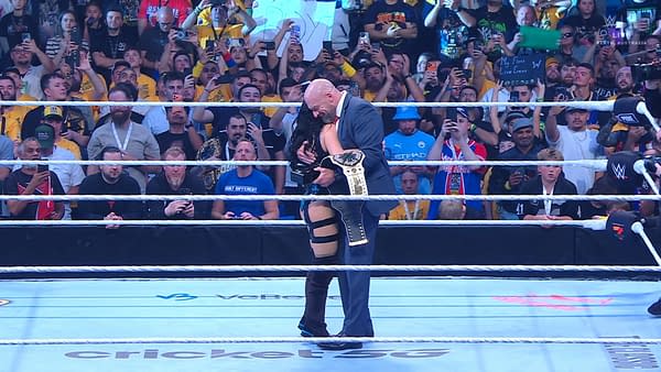Triple H embraces Stephanie Vaquer in the wrestling ring while presenting her with treasures from the Saudi Arabian royal family. A crowd of fans, some holding cameras, surrounds them.