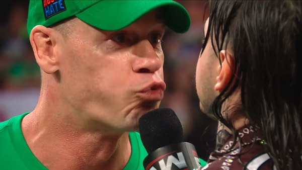 John Cena passionately speaks into a microphone while facing Dominik Mysterio, showcasing a moment of intensity during one of Cena's final appearances on WWE Raw.