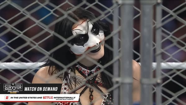 Rhea Ripley, adorned in striking face paint and spiked attire, smirks from within the confines of a steel cage during the women's WarGames match at WWE Survivor Series.