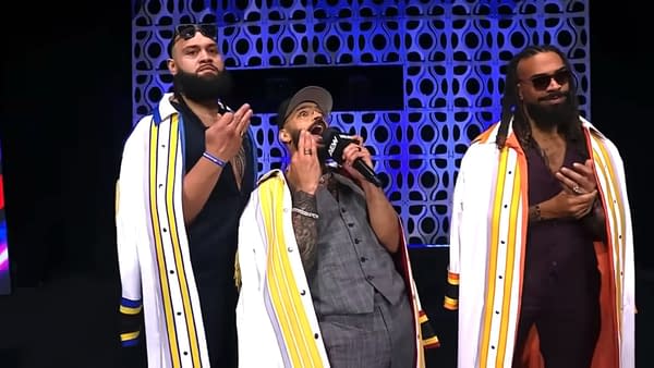 Three wrestlers on stage at AEW Dynamite, with one man passionately speaking into a microphone. They are dressed in stylish outfits with colorful accents and show a range of emotions.