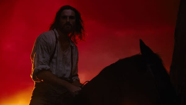 A scene from "Wuthering Heights" featuring a man with long hair in a historic shirt, sitting on a dark horse against a dramatic red and orange sky.
