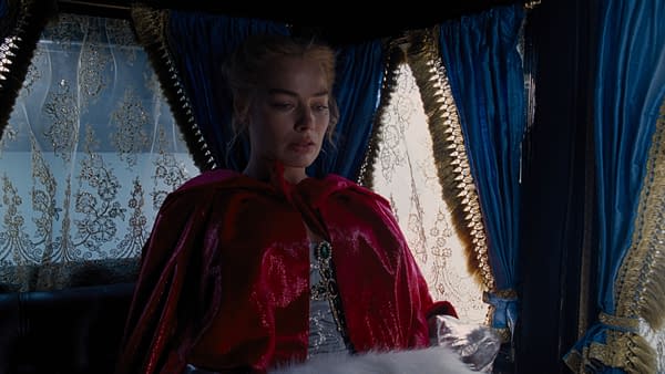 A woman in a luxurious red cloak stands in a richly decorated room with deep blue curtains and lace trim, looking thoughtfully out of a window. The scene emanates a dramatic and moody atmosphere, likely inspired by 'Wuthering Heights.'