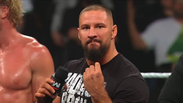Bron Breakker delivers a powerful promo on WWE Raw, holding a microphone and making a strong gesture with his hand. His focused expression and stance convey the seriousness of his message.