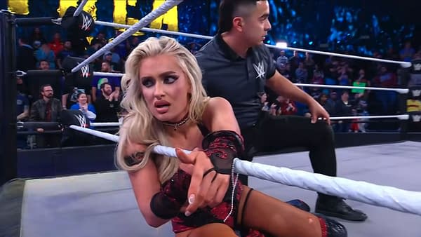 Former NXT Champion Blake Monroe displays a shocked expression while seated on the mat, clutching the ring rope, suggesting a moment of confusion following a title loss in a wrestling match, with a referee nearby and a crowd in the background.