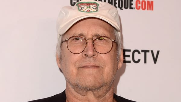A close-up photograph of Chevy Chase, who is wearing round glasses and a white baseball cap with a logo, smiling slightly. This image was taken at the premiere of 'The Last Movie Star' at the Egyptian Theater in Los Angeles.