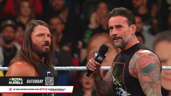 AJ Styles and CM Punk engage in a lively interaction during WWE Raw, with a captivated audience in the background. CM Punk holds a microphone, gesturing as AJ Styles looks on with a focused expression.
