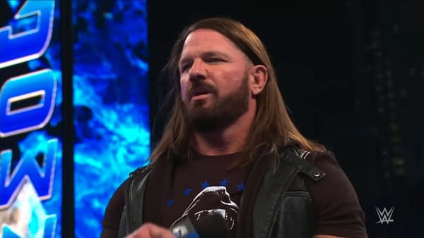 AJ Styles stands on stage during WWE SmackDown, wearing a black vest over a dark t-shirt. The blue backdrop features the WWE SmackDown logo, adding to the energy of the event.
