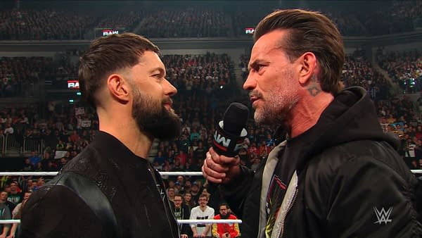 Finn Balor and CM Punk are engaged in a tense face-off, standing inches apart as CM Punk holds a microphone and speaks passionately. The live audience is visible in the background, adding to the atmosphere of the moment.