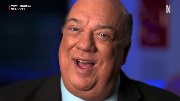 Paul Heyman, an influential figure in wrestling, smiles while wearing a suit against a soft blue background. His enthusiastic demeanor suggests a promotional context related to WWE.