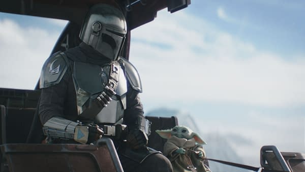The Mandalorian, wearing his signature armor, sits alongside Grogu, who has large ears and a playful expression, in a spacecraft against a backdrop of blue skies. This scene captures a moment between the two characters from Lucasfilm's 'The Mandalorian and Grogu.'