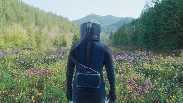 A character in a protective suit stands in a vibrant field of flowers, surrounded by lush greenery and mountains in the background, evoking a sense of exploration and adventure. This scene is connected to the film 'In The Blink Of An Eye'.