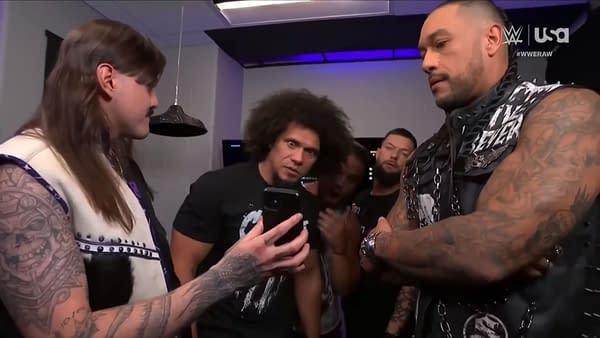In a WWE backstage scene, members of The Judgment Day group react to a surprising text displayed on a phone, showcasing their mixed expressions of shock and curiosity. The setting features modern lighting and casual attire.