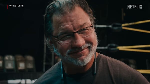 Al Snow, former WWE star, smiles while wearing glasses and a headset, with wrestling ring ropes visible in the background. He appears in a Netflix documentary about wrestling.