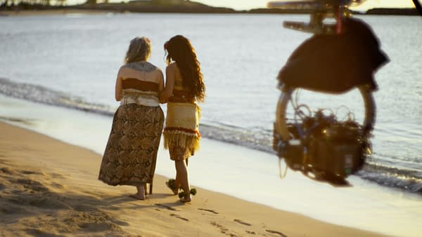 MOANA Behind-the-scenes photo from Disney's live-action Moana, featuring Rena Owen and Catherine Laga'aia walking along the beach.