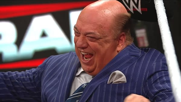 Paul Heyman is laughing joyfully while seated at a WWE Raw event, wearing a pinstriped suit and a tie. The background features WWE branding, creating an energetic atmosphere.