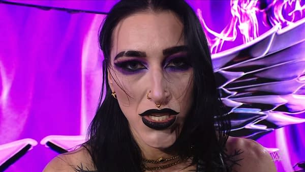 Rhea Ripley shows a fierce expression during her appearance on WWE Raw, with dramatic makeup featuring bold black lips and striking eye color against a purple background.