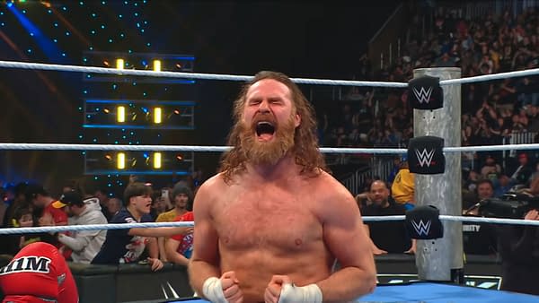 Sami Zayn, with long hair and a beard, celebrates in the wrestling ring after winning back the United States Championship during WWE SmackDown. The audience can be seen cheering behind him.
