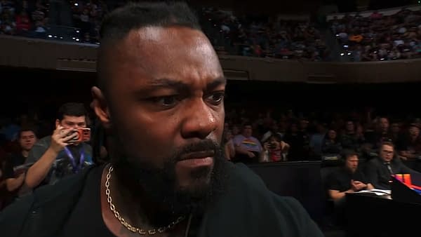 A close-up of a man with a serious expression, showing frustration or disbelief while watching AEW Dynamite. Fans and commentators can be seen in the background.