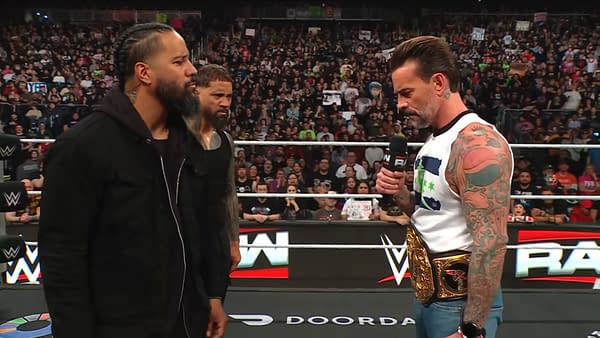 The Usos confront CM Punk in the ring during an episode of WWE Raw, with a captivated audience in the background and CM Punk holding a microphone and a championship belt.