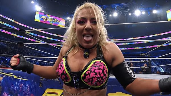 Thekla celebrates joyfully after securing the first pin in a two-out-of-three falls match, wearing a vibrant outfit and making a playful expression. The wrestling ring is illuminated with bright lights and the AEW Revolution logo is visible in the background.