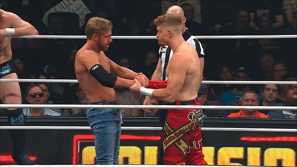 In a wrestling ring, Blake Christian holds the hands of Orange Cassidy to prevent him from putting his hands in his pockets, both wrestlers displaying serious expressions. Fans can be seen in the background, showcasing their enthusiasm.