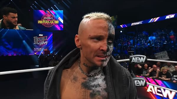 Darby Allin reacts with a serious expression as he listens to another wrestler, MJF, during an AEW Dynamite event. The backdrop features vibrant colors and promotional graphics for AEW's Spring Breakthru and Double or Nothing events.