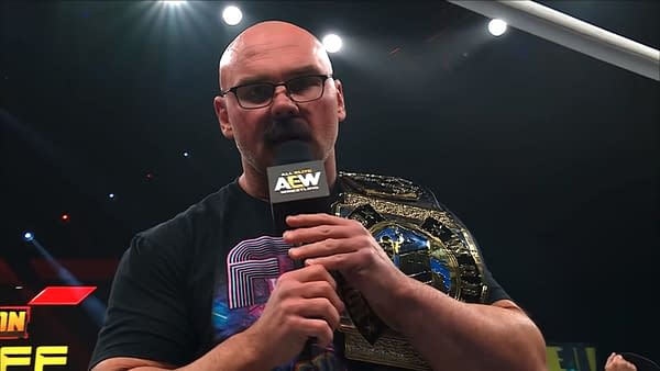 Dax Harwood speaks into an AEW microphone with a championship belt draped over his shoulder during AEW Collision.