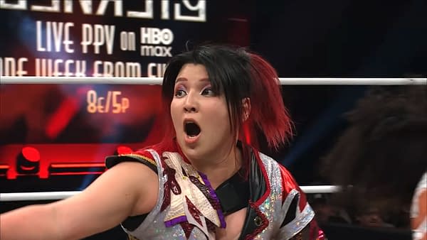 Hikaru Shida, a professional wrestler, expresses surprise in the ring during her first AEW match in over a year. She is wearing a colorful wrestling outfit with an ornate design and her hair is styled with bright red highlights.