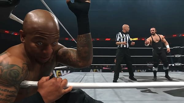 A wrestler with a bald head and distinctive tattoos makes a shocked expression while clutching the ring ropes during a match. In the background, another wrestler and a referee are engaged in the action.