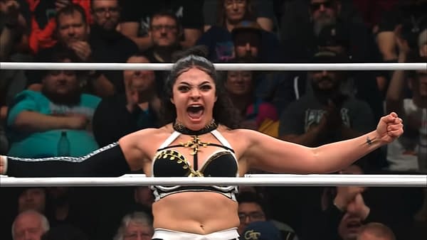 Persephone celebrates in the wrestling ring on AEW Collision, shouting with both arms spread wide. The crowd blurs in the background as she looks fired up.